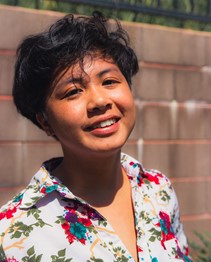 A young Filipino person with short hair wearing a collared shirt, smiling and looking at the camera