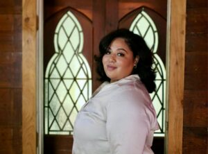 Dr. Marta Torres wears a white shirt and looks over her shoulder standing in front of decorative windows