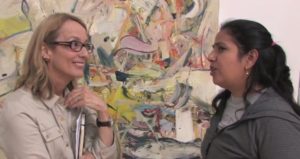 Two women standing in front of a piece of artwork in conversation.