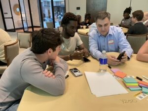 Made By Us participants sit in a workshop, engaging with an educator at a table. 