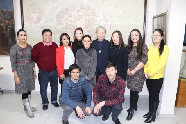 A group of individuals poses together. Nine individuals are standing at the back, and two are crouched below. Most are smiling.