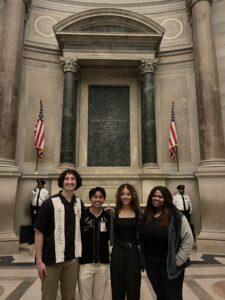 Made By Us participants, two young men of color and two young women of color, stand in front of a the US Constitution and Bill of Rights. 
