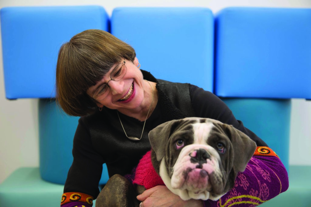 A smiling woman looks at a brownish gray and white dog, who looks up at the camera.