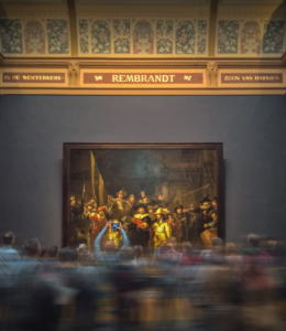 Many people rush past a large oil painting in a museum. They are moving so quickly that they become a blur.