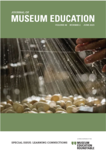 Water falls in a light sprinkle over lightly colored circular pebbles.On the upper right hand side, a hand reaches forward to touch the water before it can fall on the rocks.