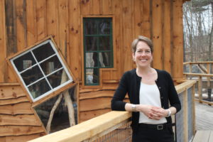Photo of Marie Beam, a white woman with short hair wearing black and white business clothes, smiling and looking at the camera, against a backdrop of wood panels