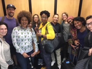 Group of people in an elevator leaning toward each other and smiling for the photographer.