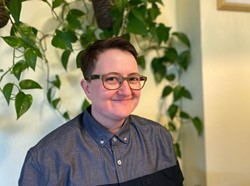 A young white person wearing glasses and a collared shirt, smiling and looking at the camera