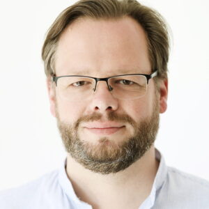 Photo of Wolfgang Schmutz a white male with a beard and glasses. He is wearing a white collared shirt.