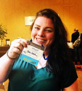An image of the author smiling while holding up her name badge from the conference.